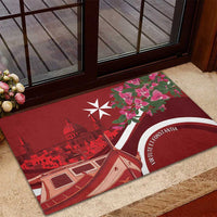 Red rubber doormat on stone step, Malta skyline, boat, pink blossoms and white emblem