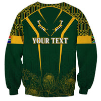 Green crewneck sweatshirt with YOUR TEXT graphic and kente-style patterns, long sleeves