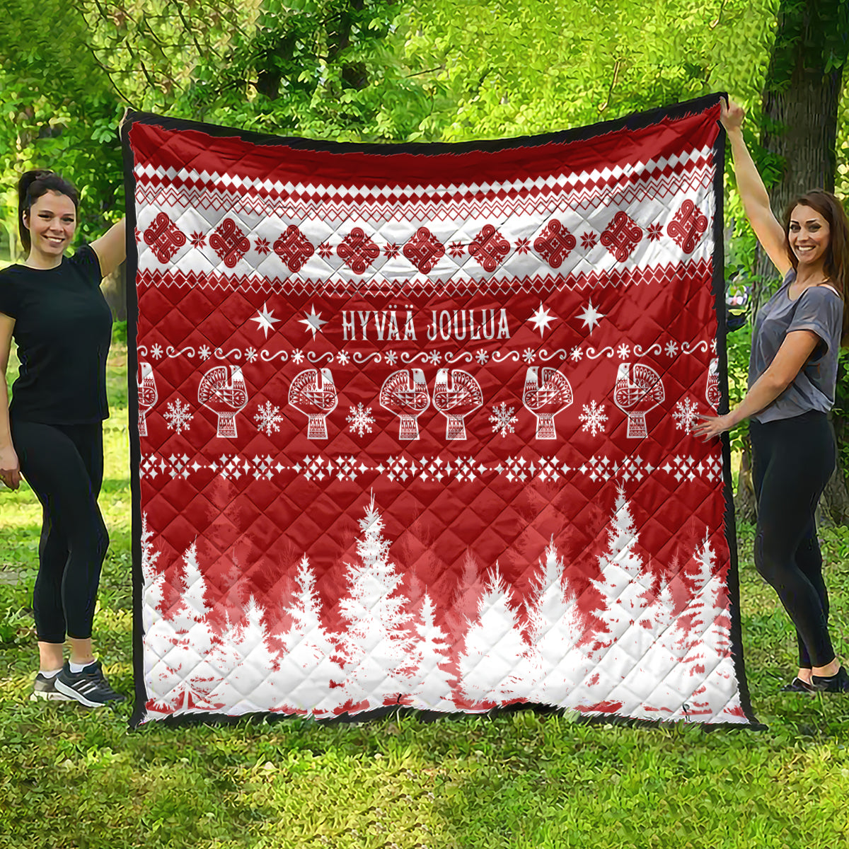 Red and white Christmas quilt spread outdoors with 'HYVAA JOULUA' and fir tree print