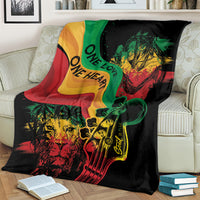Reggae-themed throw blanket on cream couch, black with “One Love” lion, guitar, and reggae flag colors.