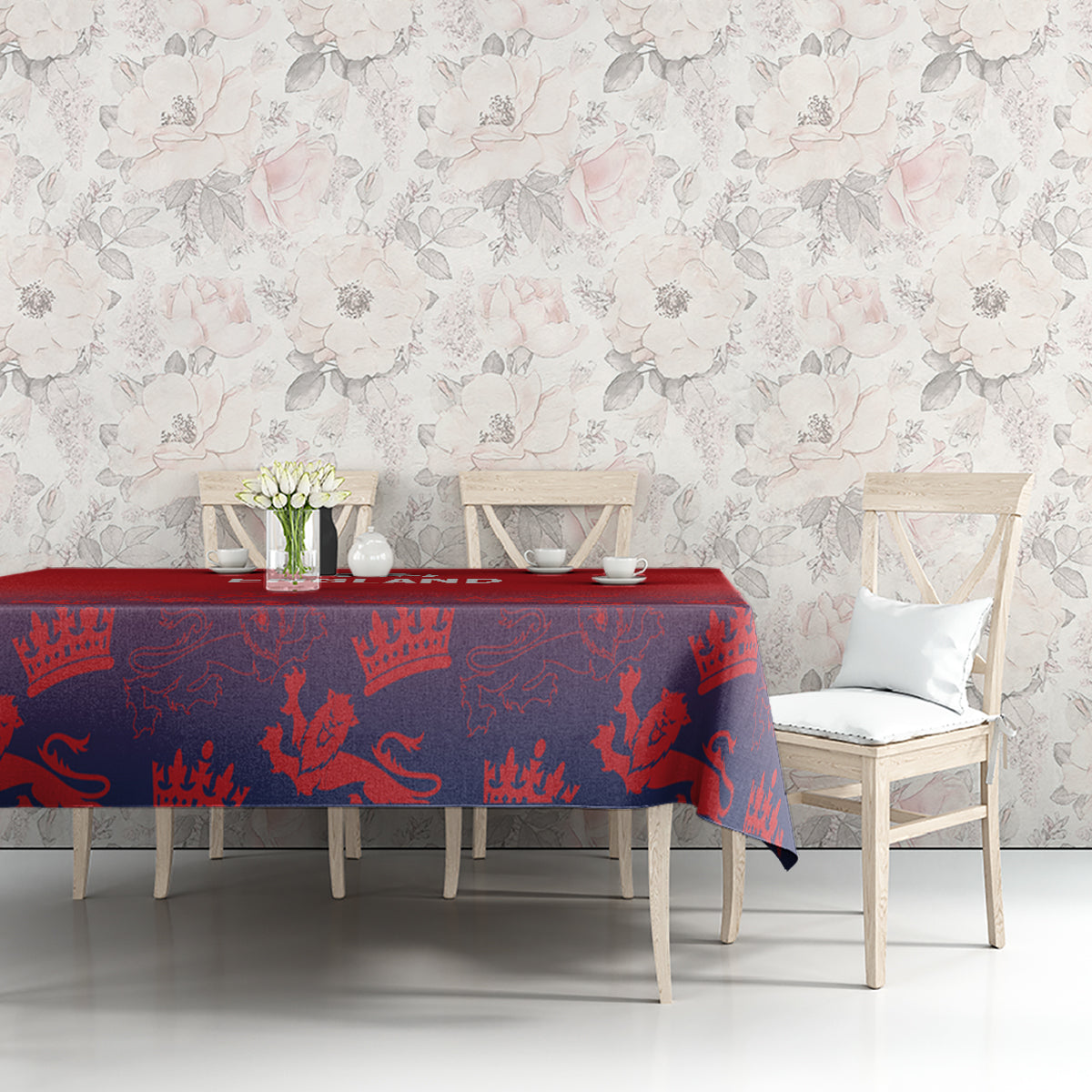 Red and navy crown-patterned tablecloth on dining table with cups and vase.