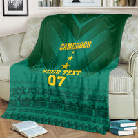 Green Cameroon blanket draped on couch, showing “CAMEROON”, stars, “YOUR TEXT”, “07”
