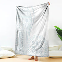 White blanket with light-blue traditional pattern, draped over a bed.