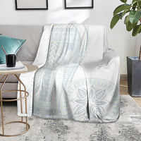 White blanket with light-blue geometric leaf pattern, laid over a sofa.