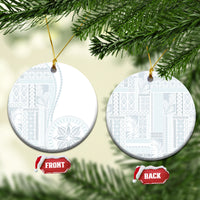 White ceramic round ornament with blue patterned siapo design, hanging on gold cord.