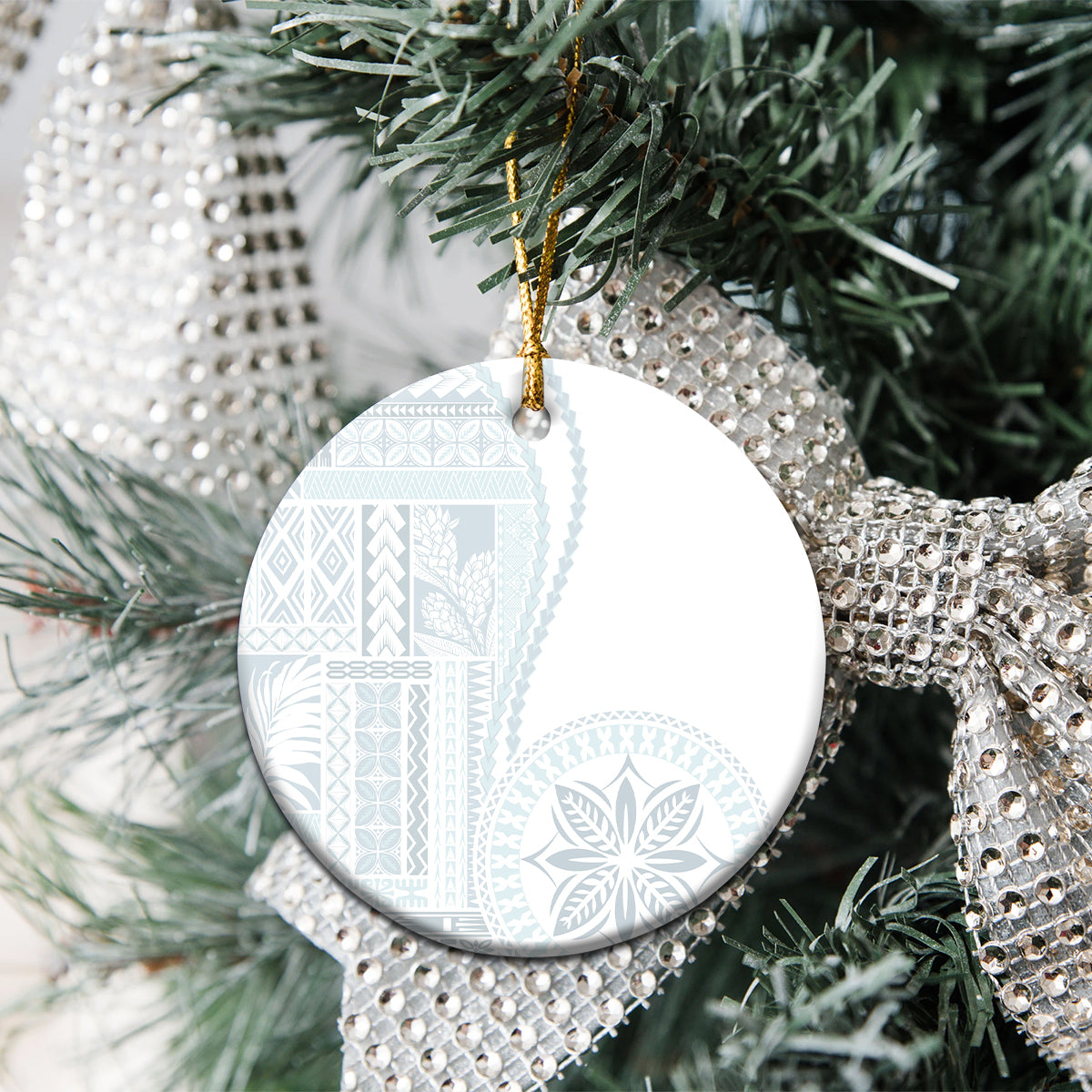 White ceramic round ornament with blue patterned siapo design hanging on Christmas tree.