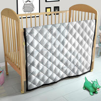 White diamond-quilted baby blanket with dark edge trim on wooden crib