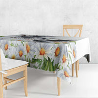 White tablecloth with orange daisy blossoms and green leaves, hanging over bench.