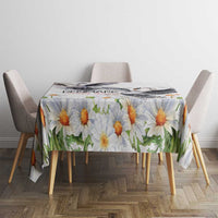 White tablecloth with muted daisy flowers, green leaves, and orange-yellow blossoms.