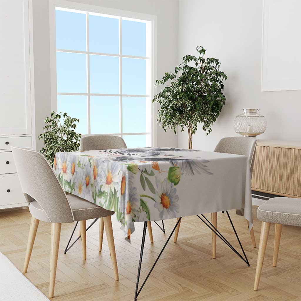 White floral tablecloth with orange-yellow daisies and green leaves, neatly draped.