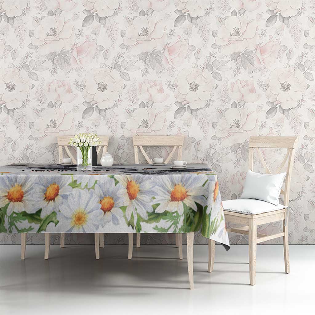 White tablecloth with large orange and yellow daisy blooms and green leaf sprigs.