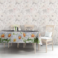White tablecloth with large orange and yellow daisy blooms and green leaf sprigs.