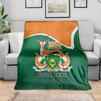 Personalized blanket folded on sofa, green front and orange top edge, crest and 'YOUR TEXT'