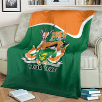 Personalized blanket on couch, green with orange top panel, central crest and 'YOUR TEXT'