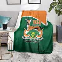 Personalized blanket on chair area, green with orange top, crest graphic and 'YOUR TEXT'