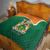 Green quilted throw quilt with orange top, emblem and 'YOUR TEXT' on a bed