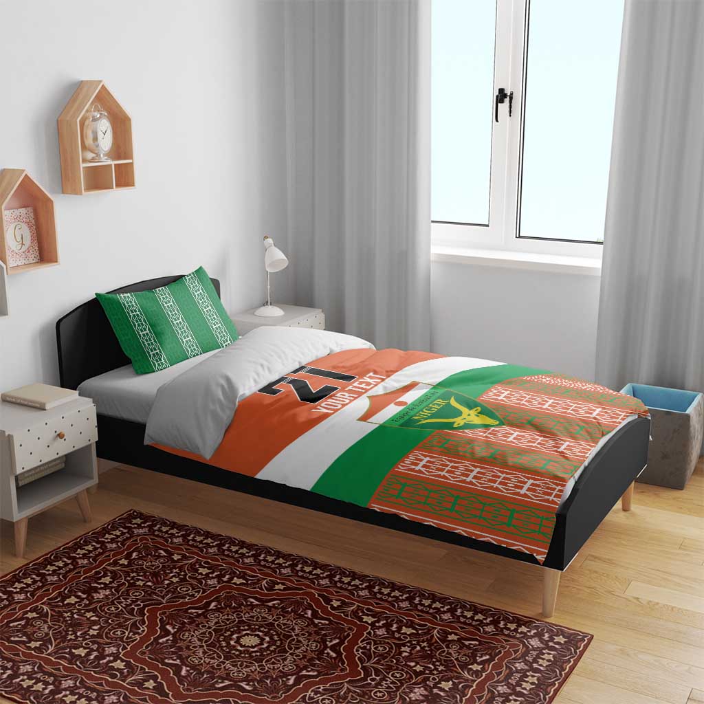 Custom bedding set on bed with orange/green/white duvet, Niger emblem, and patterned border