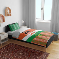 Custom bedding set on bed with orange/green/white duvet, Niger emblem, and patterned border