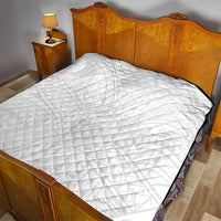 White quilt with diamond quilting pattern laid on bed with black edge trim.