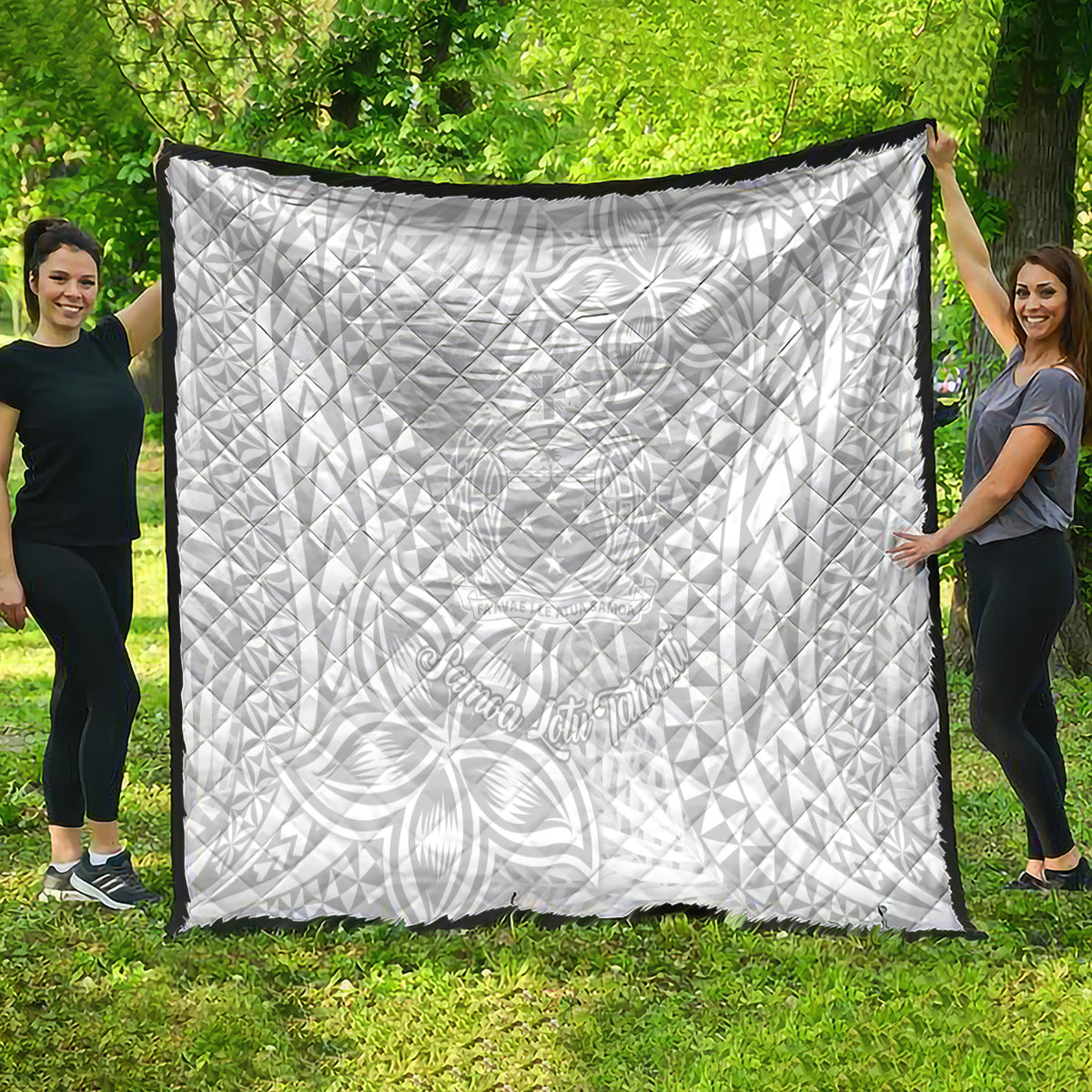 White quilt with black border, laid out outdoors, featuring tropical Polynesian pattern