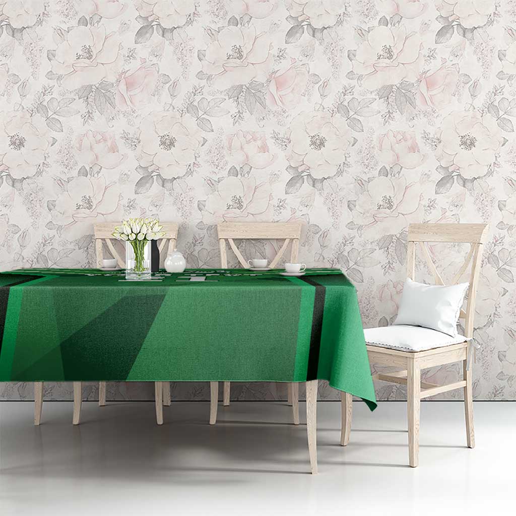Green tablecloth with sporty pattern over dining table with chairs and decor.