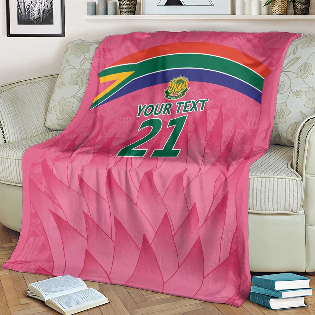 Pink custom cricket blanket with YOUR TEXT 21 and rainbow stripe band on armchair