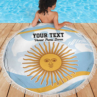 Round light blue beach blanket with fringe, sun face graphic and text, on wooden deck.