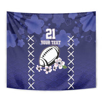 Blue tapestry wall hanging close-up showing rugby ball, sakura flowers, and rising-sun wave pattern.
