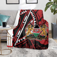 Red and black lions crest blanket with geometric pattern, laid over grey sofa