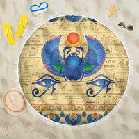 Beige round beach blanket with fringe edge and blue winged scarab emblem