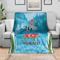 Personalized blue throw blanket draped on gray sofa, map graphic and 20 Yanvar 1990 text