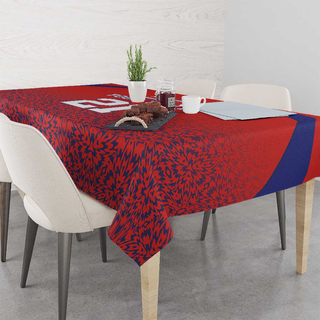 Red tablecloth with blue accent stripe and dense black-red pattern, draped over dining table.