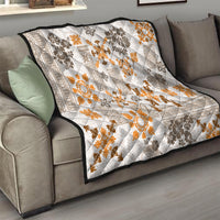 Quilt draped over gray sofa, white with orange floral tapa and dark geometric motifs