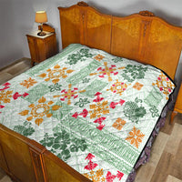 Green Hawaiian quilt blanket on bed, patterned with tapa tribal florals in orange and red