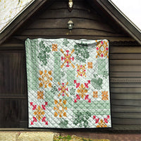Green Hawaiian tapa quilt hanging indoors, with white ground and orange and red motif designs