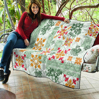 Green Hawaiian quilt spread on couch, showing tapa tribal florals in orange, red, and green