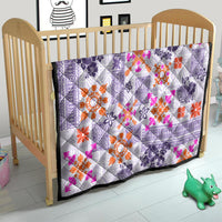 Violet quilt on a crib with white tribal tapa geometry and orange and pink floral details
