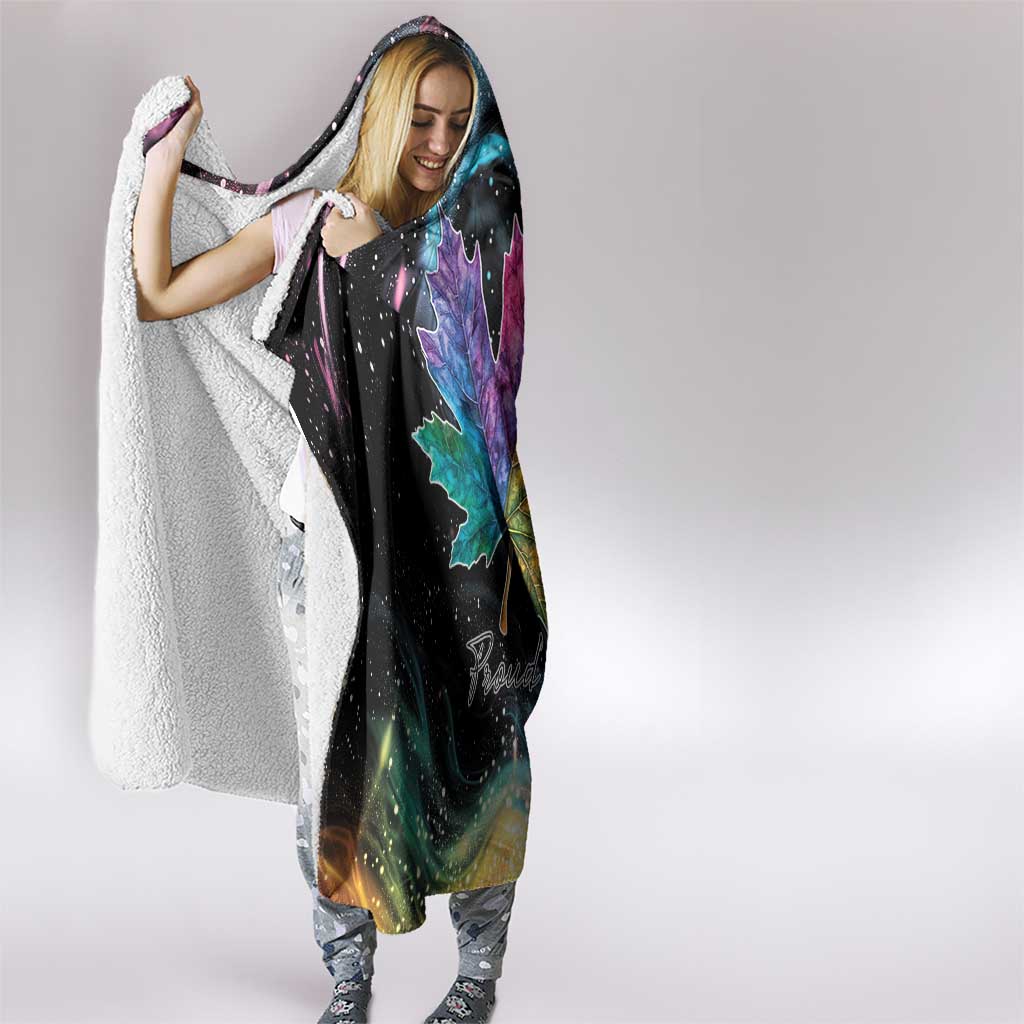 Black hooded blanket with rainbow maple leaf print and white sherpa edge, draped on person