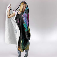 Black hooded blanket with rainbow maple leaf print and white sherpa edge, draped on person