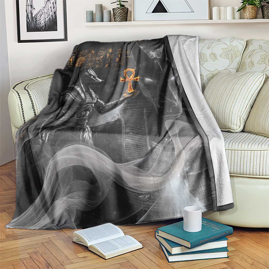 Black mythical Anubis-themed throw blanket with stylized figure and orange symbol, draped on couch