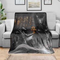 Black mythical Anubis blanket folded over a gray sofa, with orange symbol centerpiece