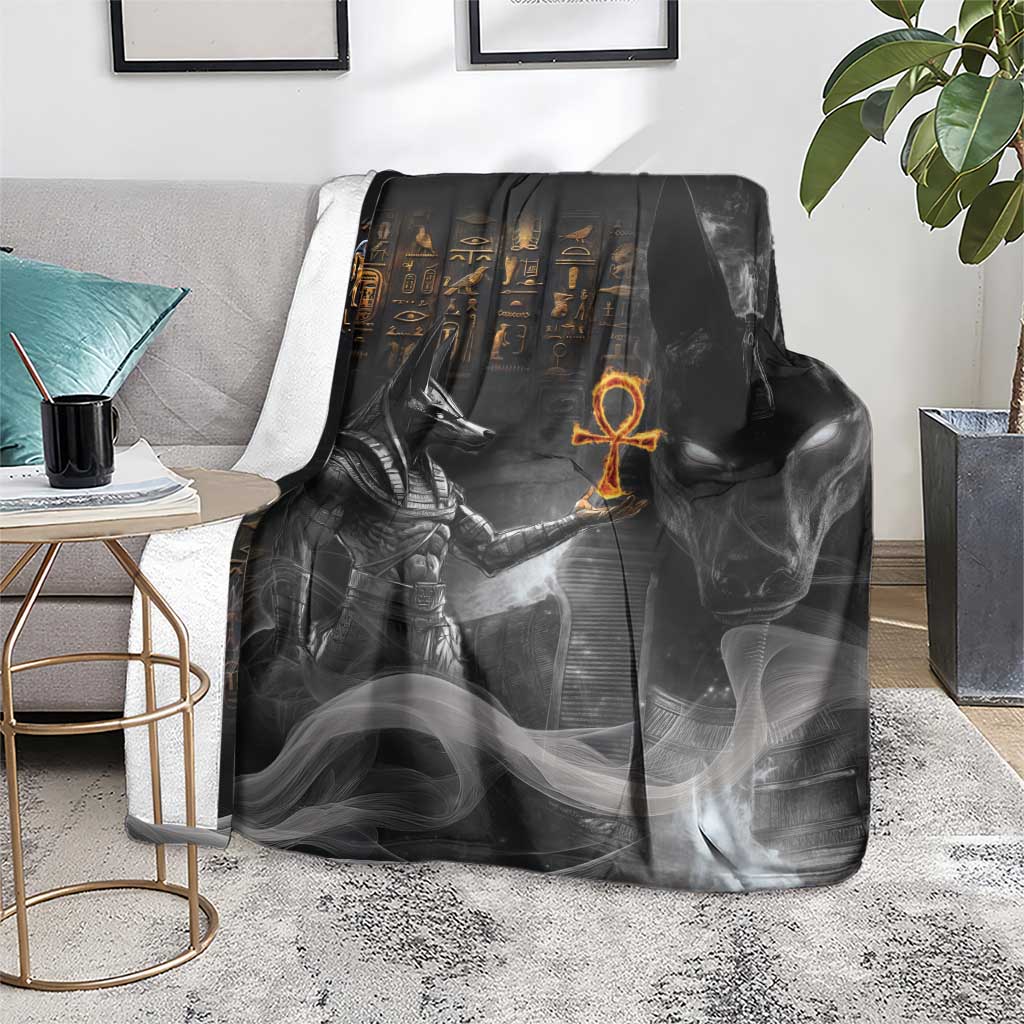 Black mythical Anubis throw blanket laid over a gray sofa seat, orange symbol in center