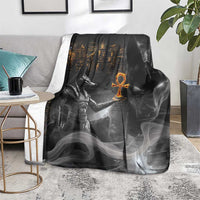 Black mythical Anubis throw blanket laid over a gray sofa seat, orange symbol in center
