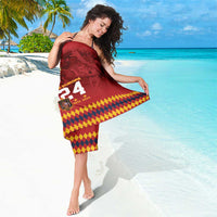 Red sarong wrap featuring 2024 and checkered yellow-purple hem graphic on beach.