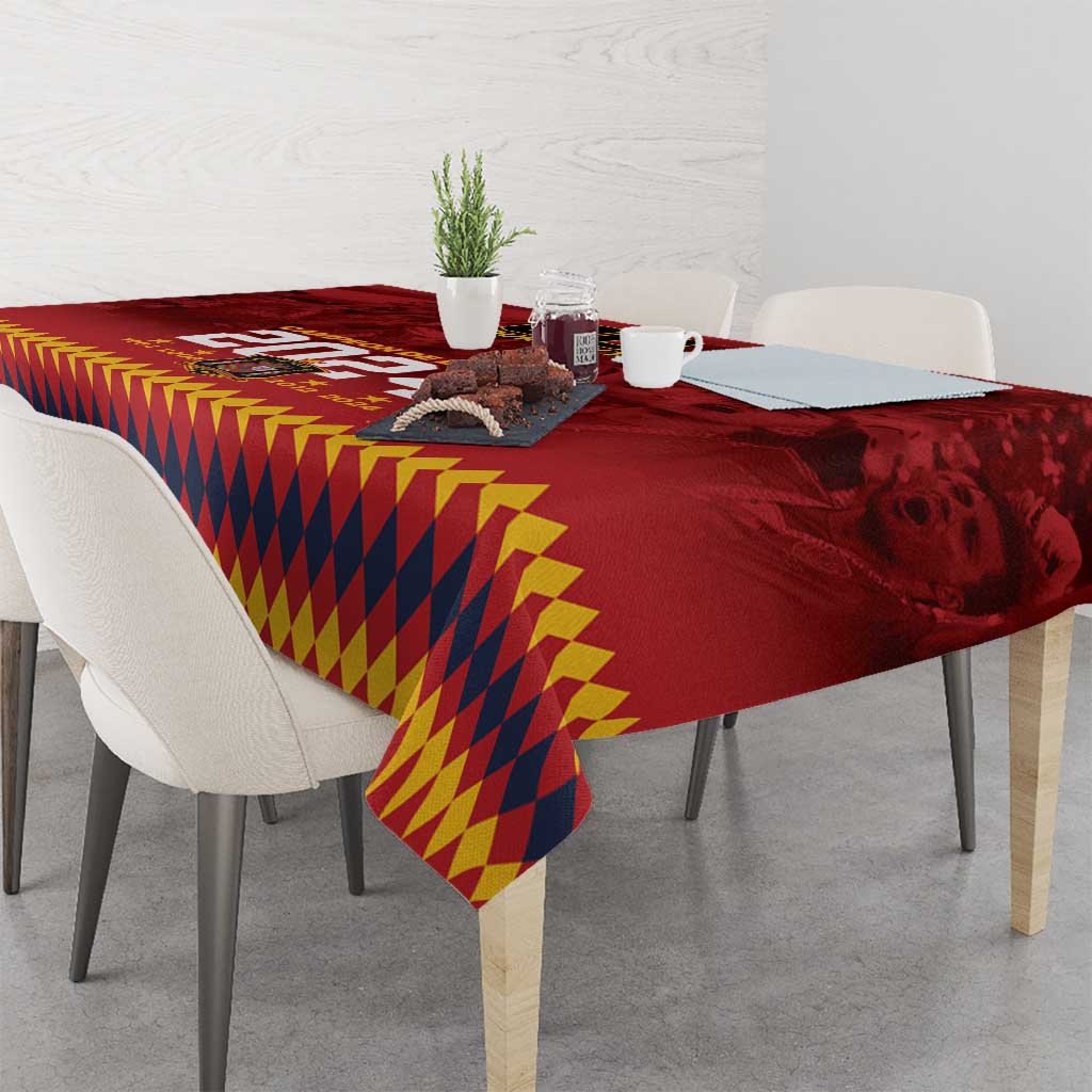Red tablecloth with yellow-and-navy geometric diamond pattern and printed crest on the edge