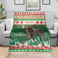 Green moose Christmas blanket draped on a sofa, red/white maple leaf stripes