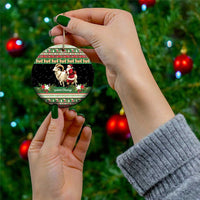Round green ceramic ornament with goat and Santa held by a hand on a Christmas tree.