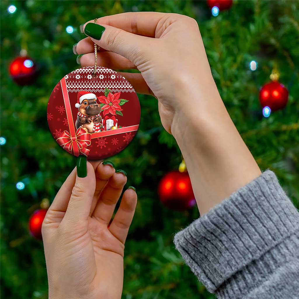 Red round ceramic Christmas ornament held by hand, cartoon cow in Santa hat and ribbon bow