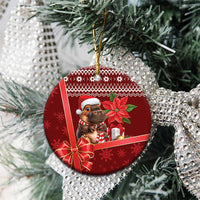 Red round ceramic Christmas ornament on evergreen branch, cartoon cow with Santa hat and bow