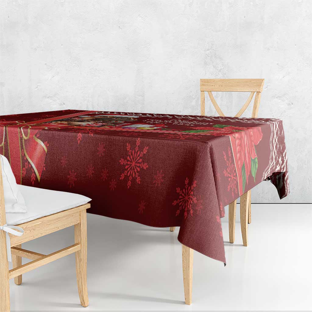 Red Christmas tablecloth draped over table edge with snowflake and ribbon design.